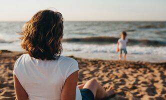 Frau am Strand beobachtet ihr Kind und genießt ihre perfekte Sehkraft